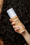 Bottle of Curl Shaper Memory Maker 3-in-One Revitalizing Milk being held against a beige background